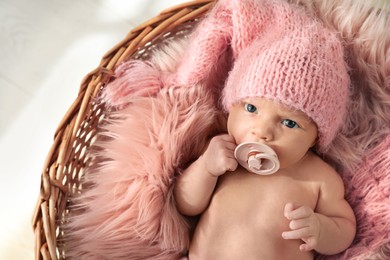 Photo of Adorable newborn baby with pacifier in wicker basket, top view