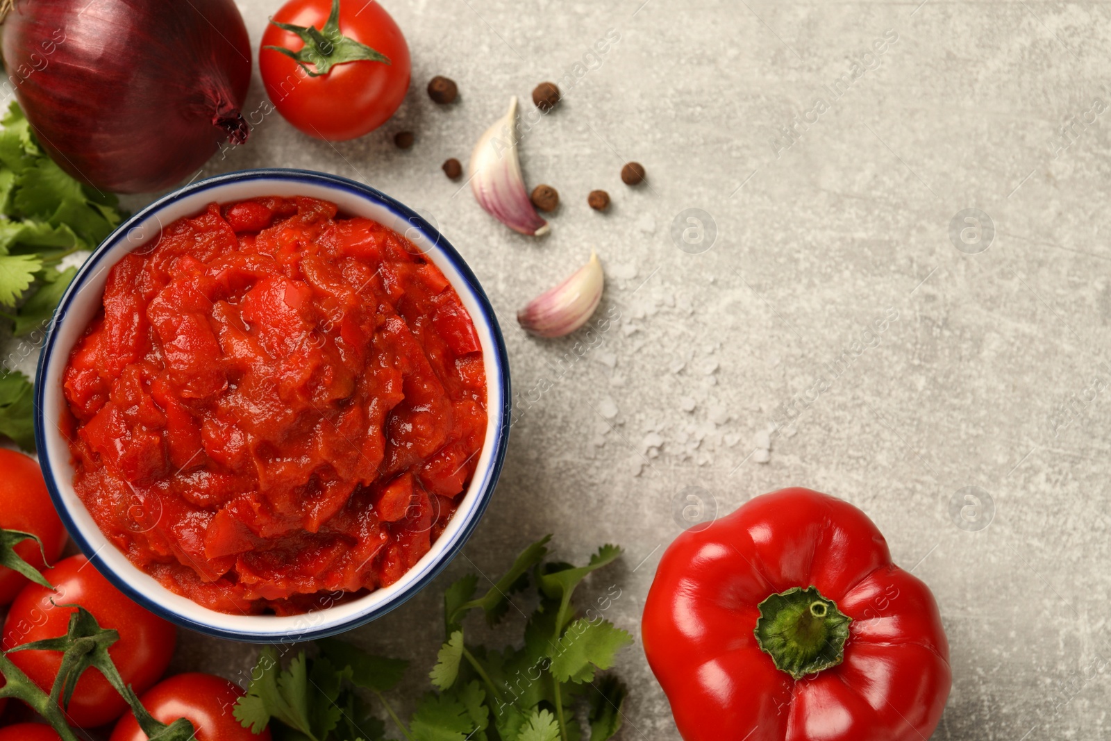 Photo of Delicious lecho in bowl and fresh ingredients on light grey table, flat lay. Space for text