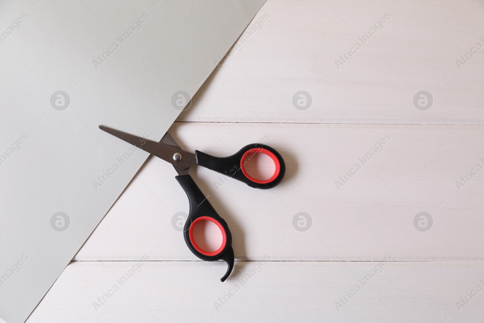 Photo of Scissors and paper on white wooden background, top view. Space for text