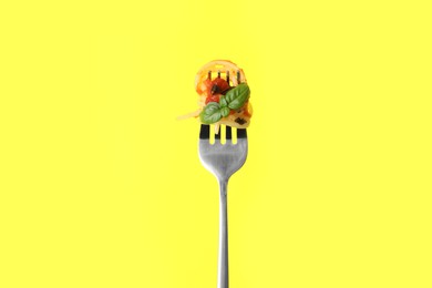 Fork with tasty pasta, basil and sauce on yellow background