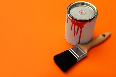Photo of Can of orange paint and brush on color background. Space for text