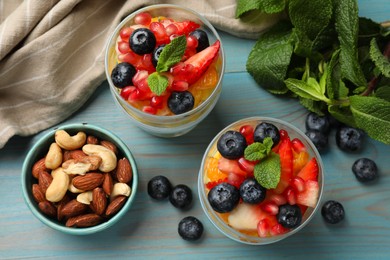 Photo of Delicious fruit salad in glasses, nuts, fresh berries and mint on light blue wooden table, flat lay