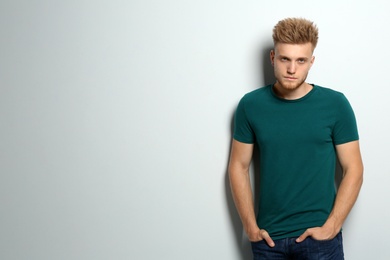 Young man wearing blank t-shirt on light background. Mockup for design