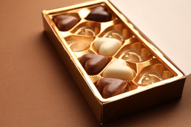 Photo of Partially empty box of chocolate candies on brown background, closeup. Space for text