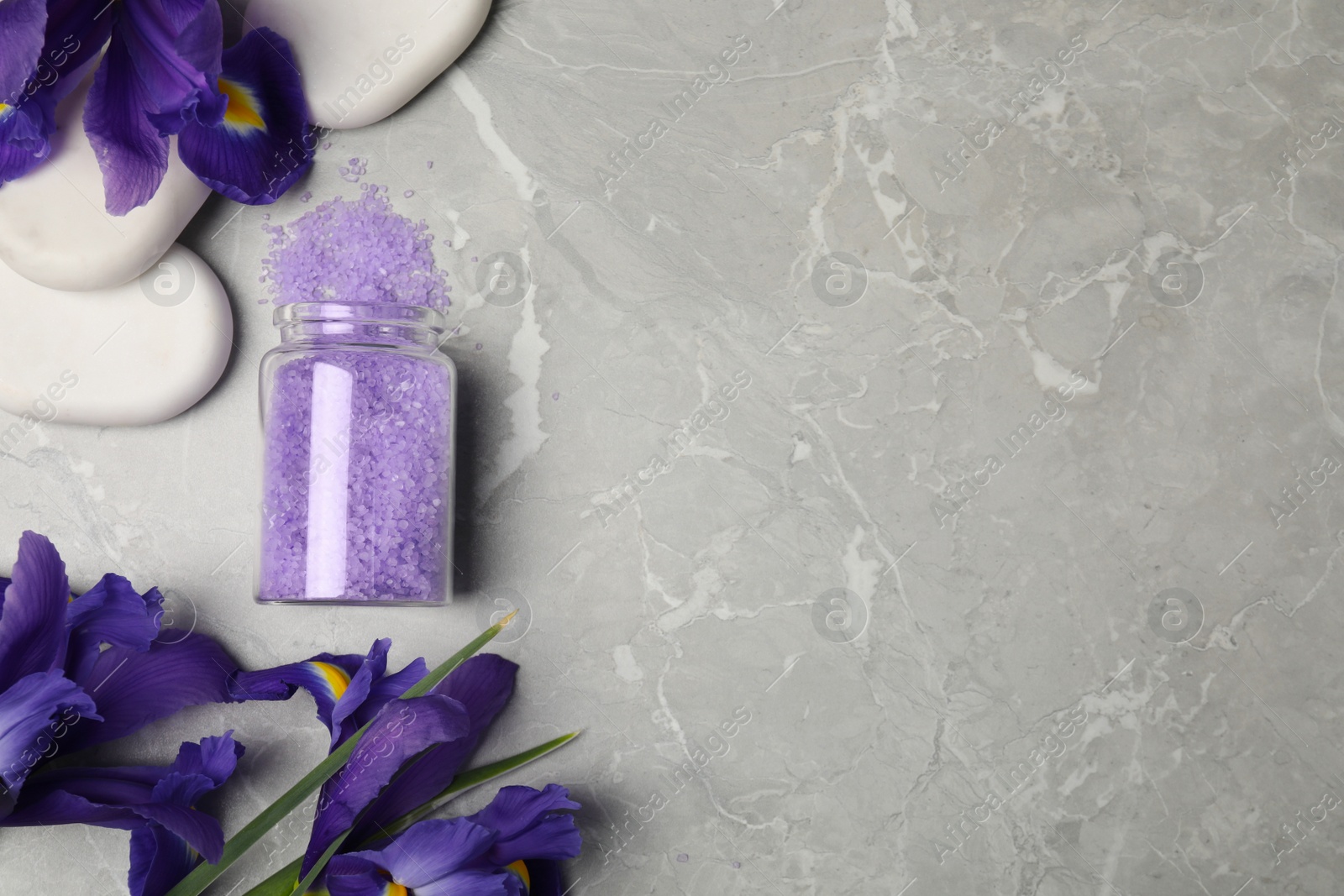 Photo of Jar with purple sea salt, spa stones and beautiful flowers on grey marble table, flat lay. Space for text