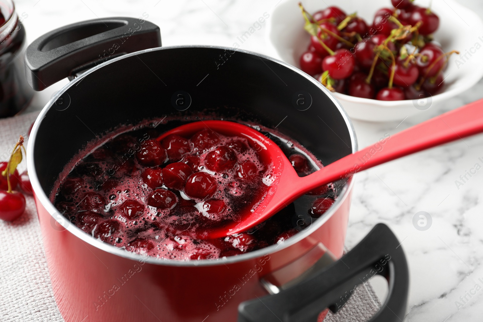 Photo of Pot with cherries in sugar syrup on table, closeup. Making delicious jam