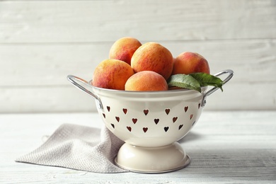 Photo of Colander with delicious ripe peaches on table