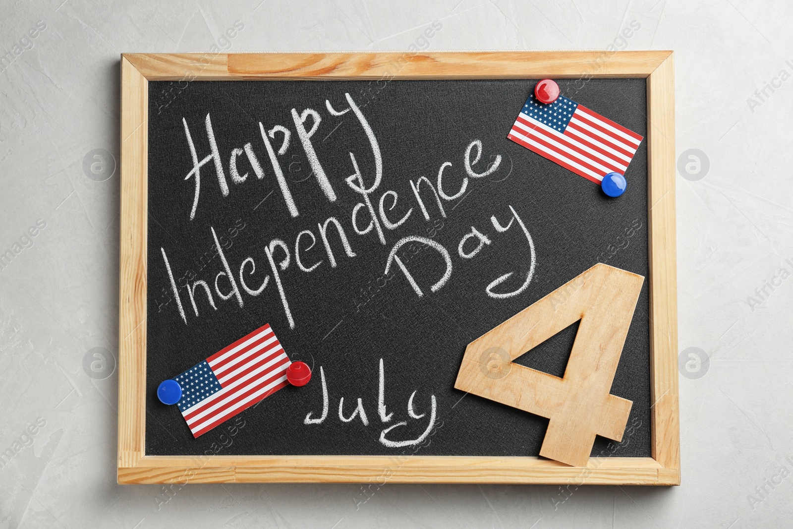 Photo of Blackboard with text Happy Independence Day, wooden number and USA flags on light background