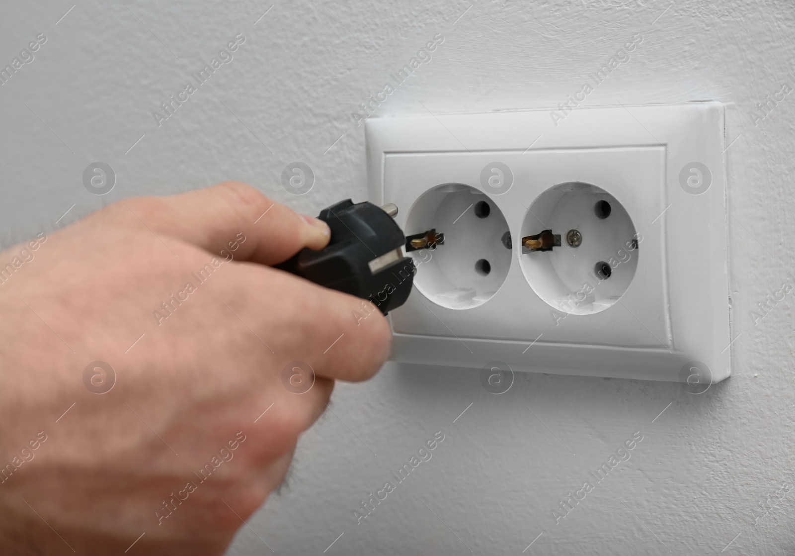 Photo of Electrician inserting plug into power socket on white background, closeup