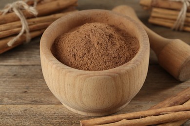 Photo of Aromatic  cinnamon powder in mortar, sticks and pestle on wooden table, closeup