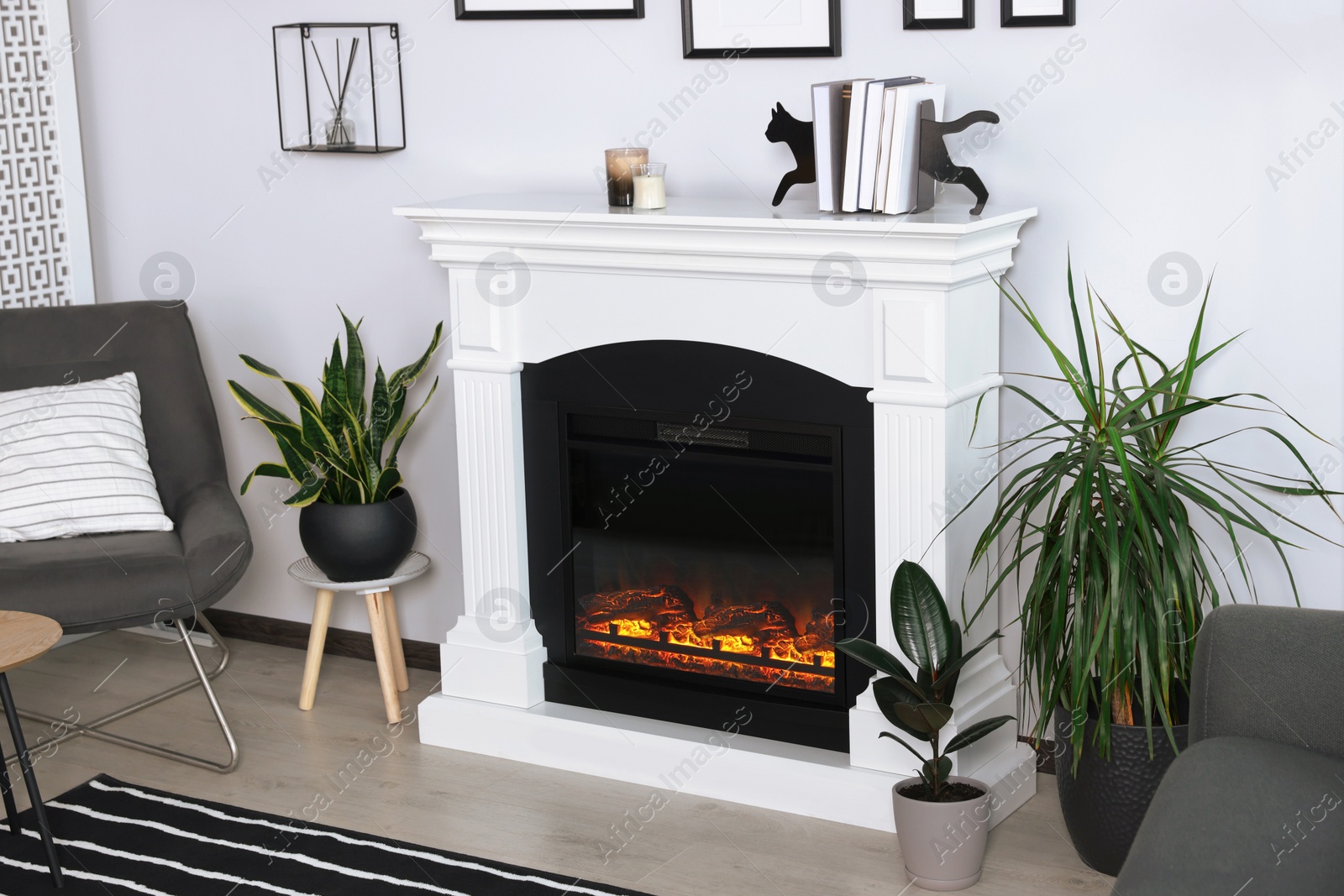 Photo of Stylish living room interior with fireplace, houseplants and grey armchair