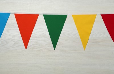 Photo of Bunting with colorful triangular flags on white wooden background