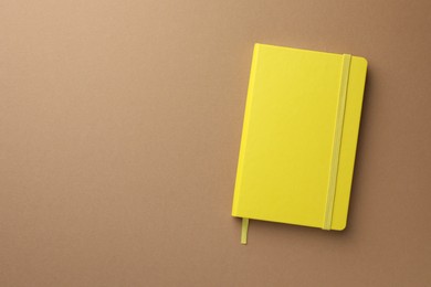 Photo of Closed yellow notebook on light brown background, top view. Space for text