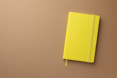 Closed yellow notebook on light brown background, top view. Space for text