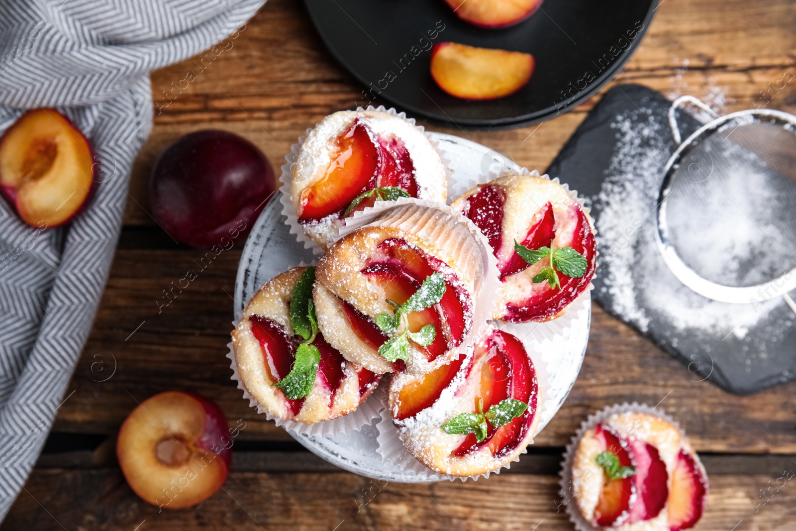 Photo of Delicious sweet cupcakes with plums on wooden table, flat lay