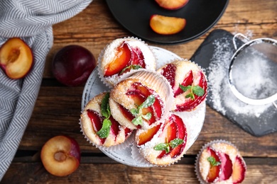 Delicious sweet cupcakes with plums on wooden table, flat lay