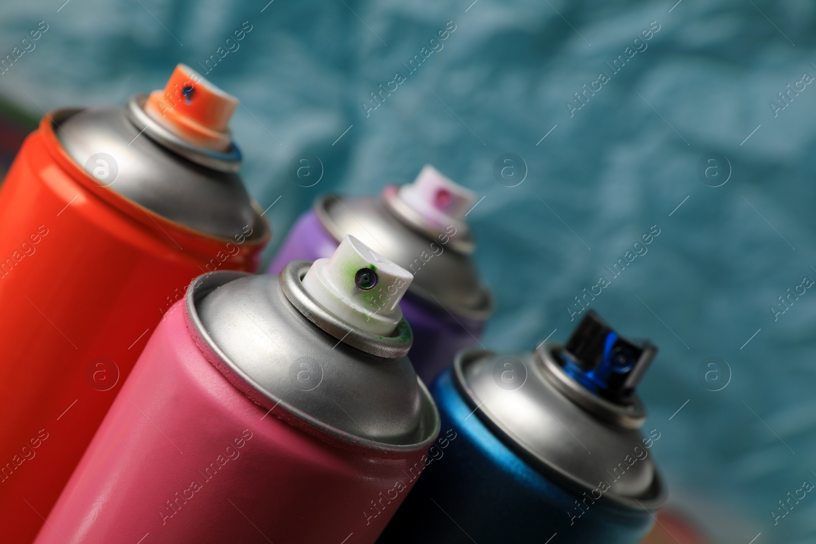 Photo of Cans of different graffiti spray paints on blurred background, closeup