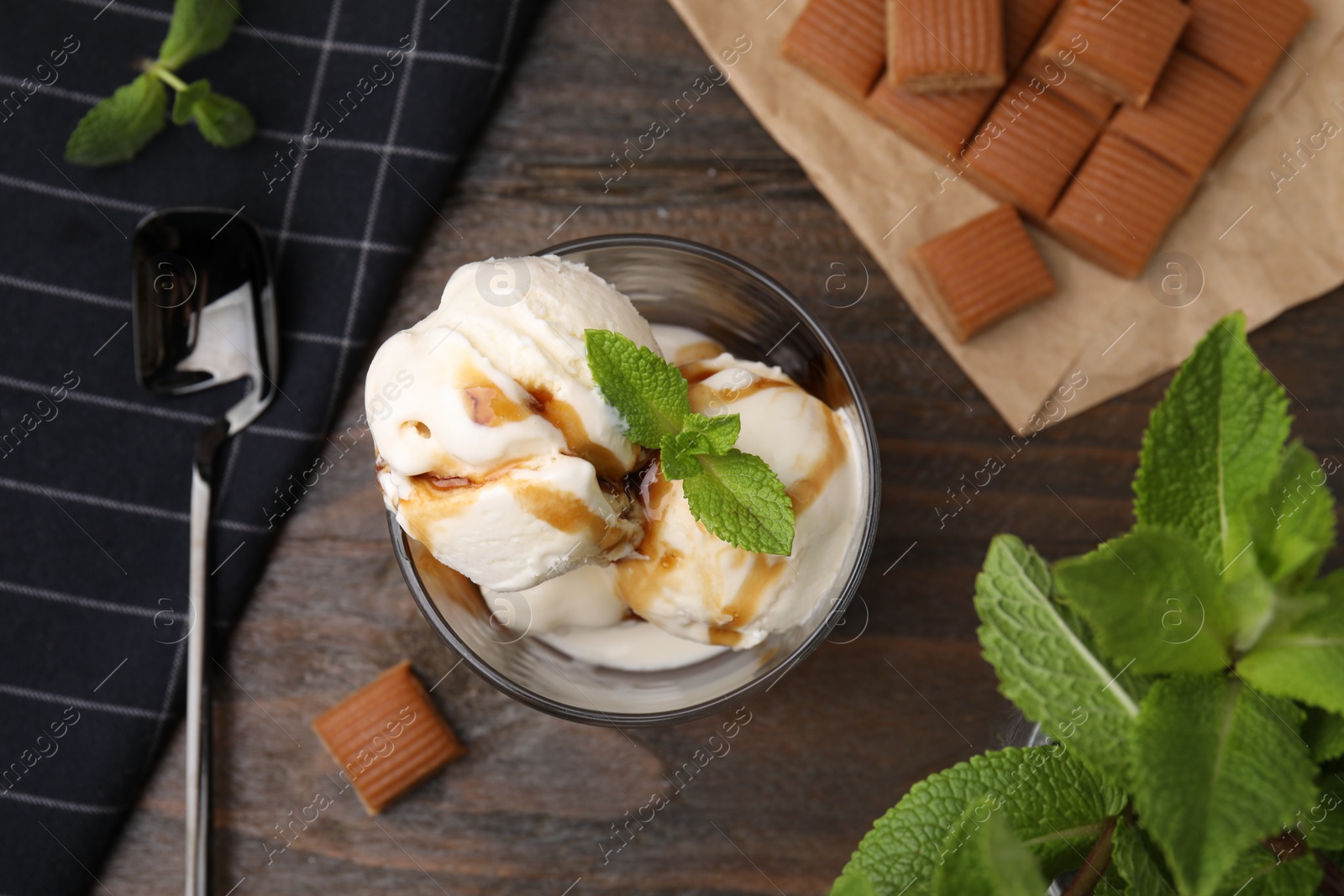 Photo of Scoops of ice cream with caramel sauce, mint leaves and candies on wooden table, flat lay