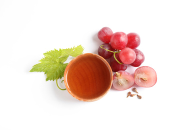 Photo of Organic red grapes, seeds and bowl of natural essential oil on white background, flat lay