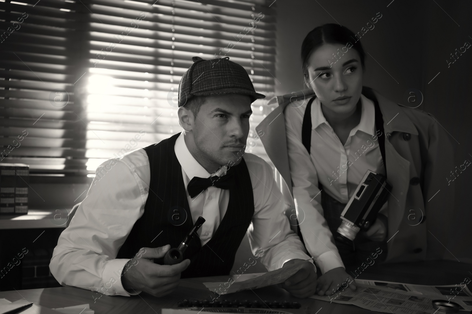 Photo of Old fashioned detective with his colleague working in office. Black and white effect