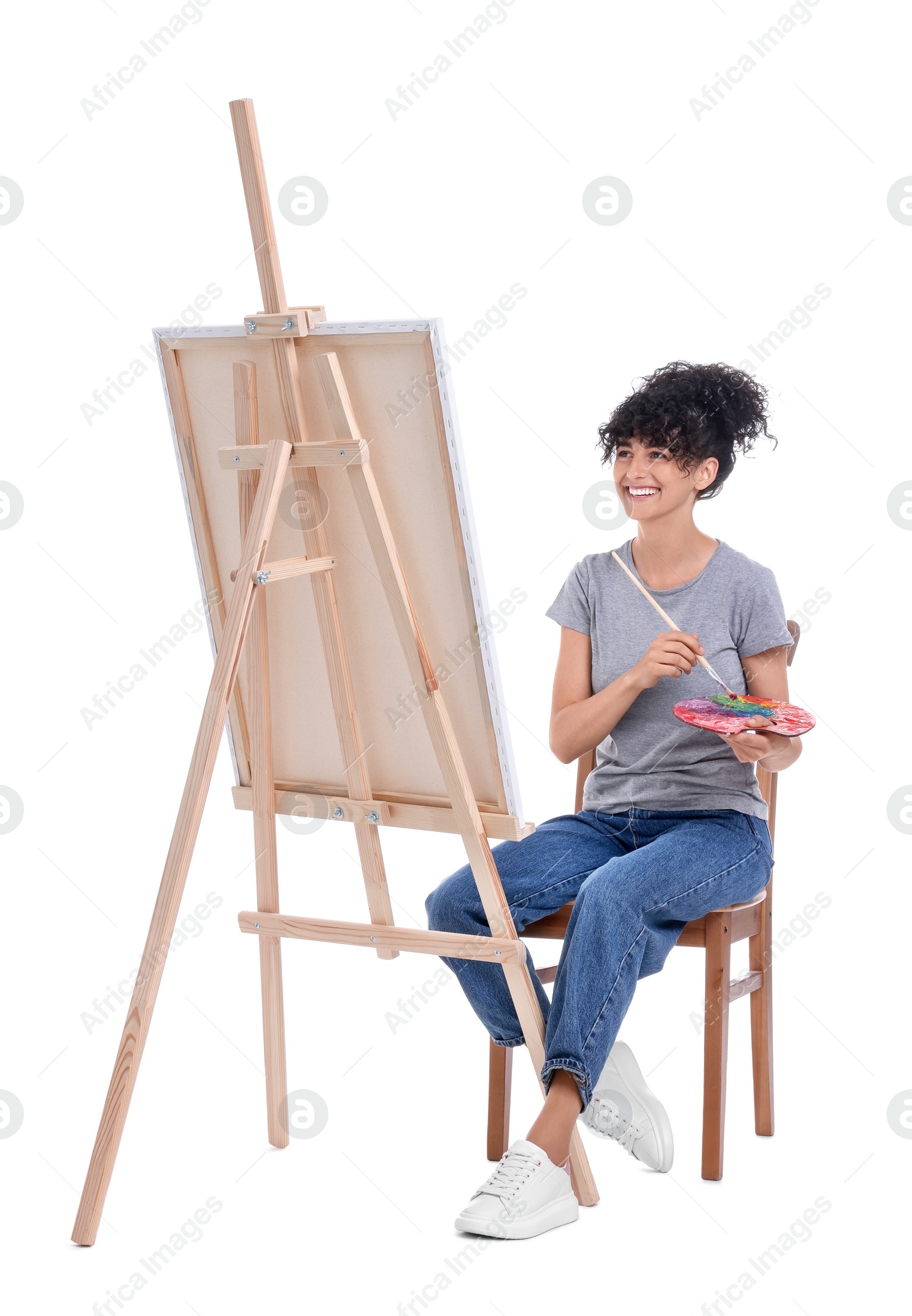 Photo of Young woman painting on easel with canvas against white background