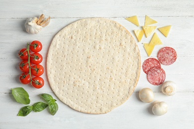 Photo of Flat lay composition with base and ingredients for pizza on light wooden table