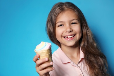 Cute little girl with delicious ice cream against color background, space for text