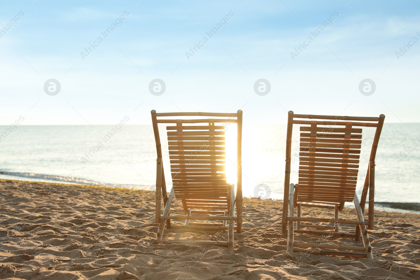 Photo of Wooden deck chairs on sandy beach. Summer vacation
