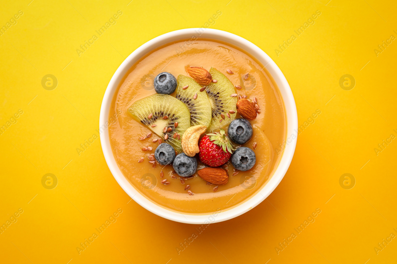 Photo of Delicious smoothie bowl with fresh berries, kiwi and nuts on orange background, top view