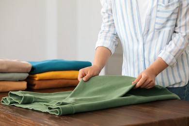 Photo of Woman folding clothes at wooden table indoors, closeup