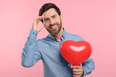 Photo of Happy man holding red heart shaped balloon on pink background