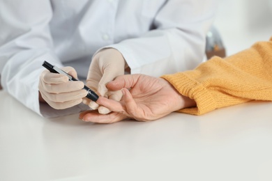 Doctor taking patient's blood sample with lancet pen in hospital, closeup. Diabetes control