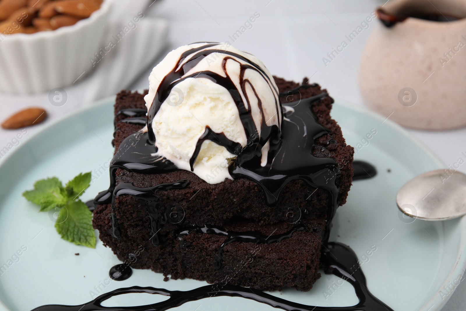 Photo of Tasty brownies served with ice cream and chocolate sauce on table, closeup