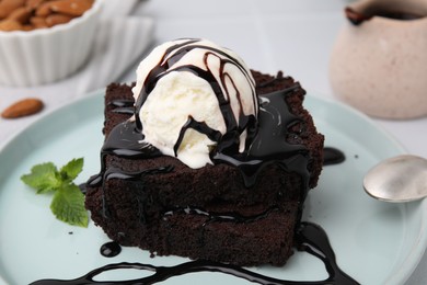 Tasty brownies served with ice cream and chocolate sauce on table, closeup