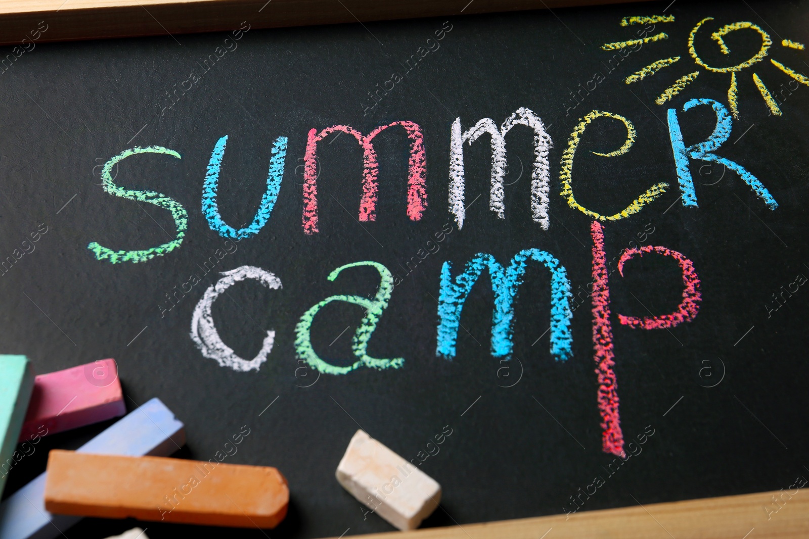 Photo of Chalk sticks on small blackboard with text SUMMER CAMP and drawing, closeup