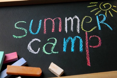 Chalk sticks on small blackboard with text SUMMER CAMP and drawing, closeup