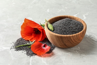 Wooden bowl of poppy seeds and flower on grey table