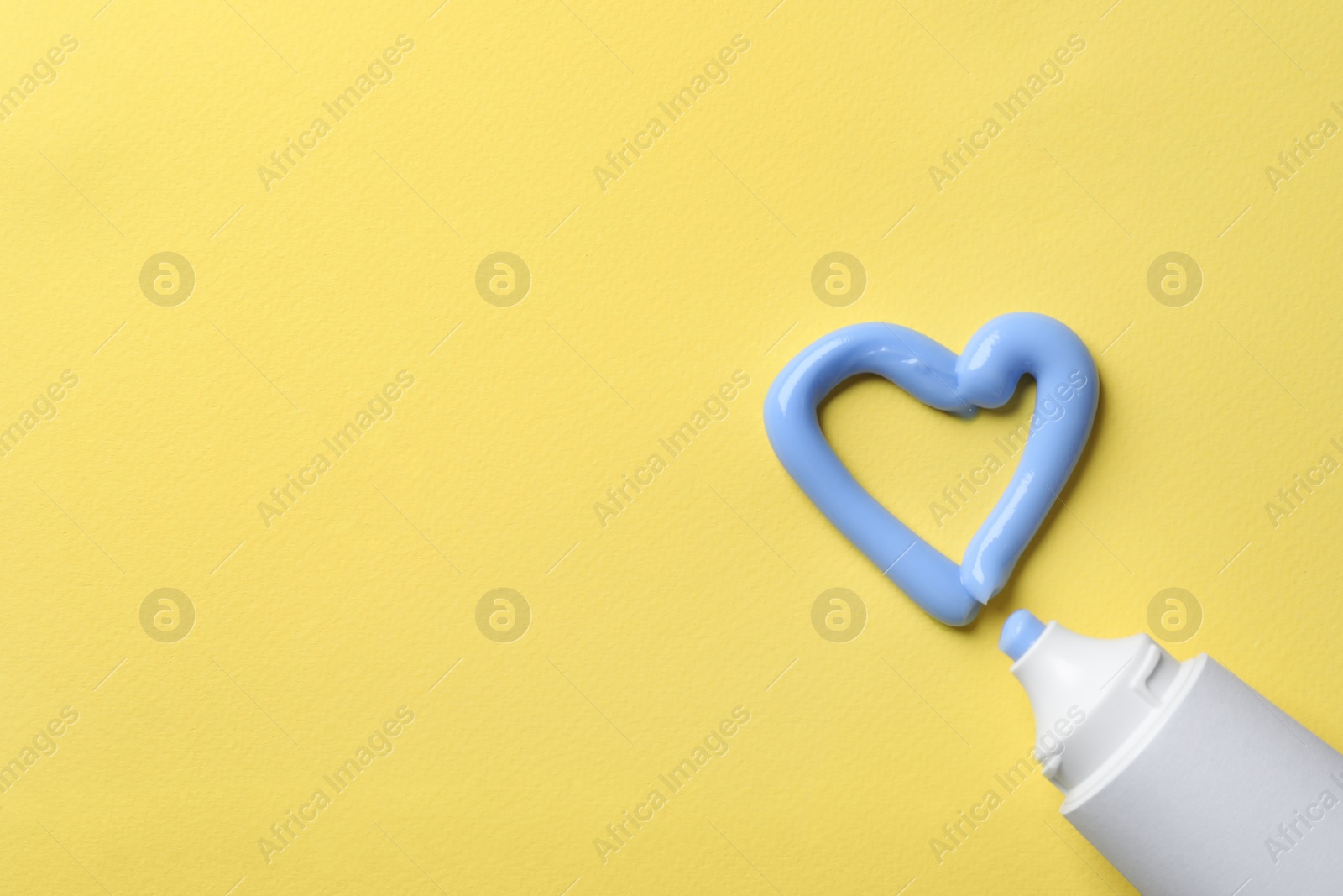 Photo of Blank tube and heart made with toothpaste on yellow background, flat lay. Space for text