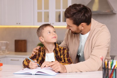 Dyslexia problem. Father helping son with homework at table in kitchen