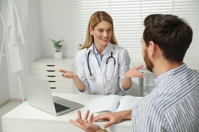 Photo of Happy doctor consulting patient at white table in clinic