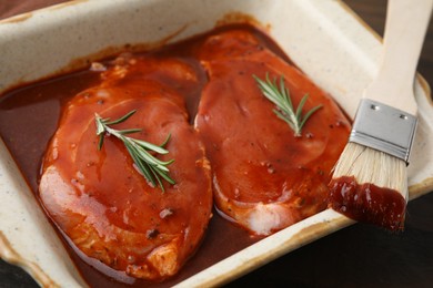 Photo of Raw marinated meat, rosemary and basting brush on table, closeup