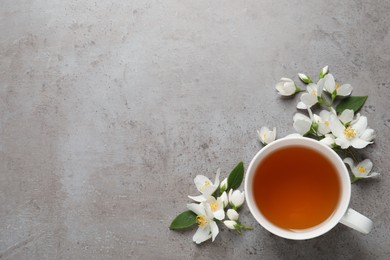 Cup of aromatic jasmine tea and fresh flowers on grey table, flat lay. Space for text