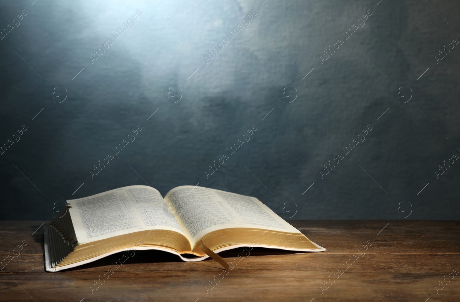 Photo of Open Bible on wooden table against color background. Christian religious book