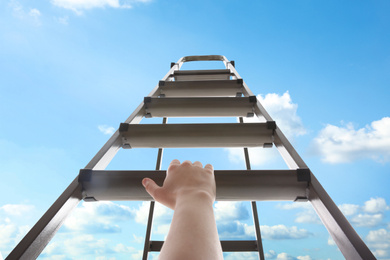Image of Woman climbing up stepladder against blue sky with clouds, closeup