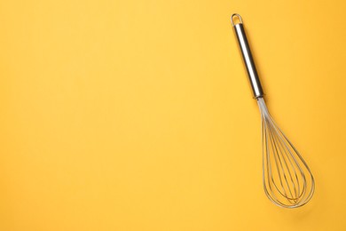 Metal whisk on yellow background, top view. Space for text
