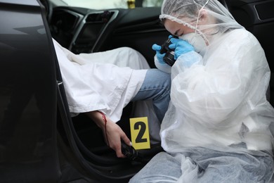 Photo of Criminologist taking photo of evidence at crime scene with dead body in car