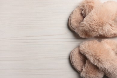 Pair of soft slippers on white wooden floor, top view. Space for text