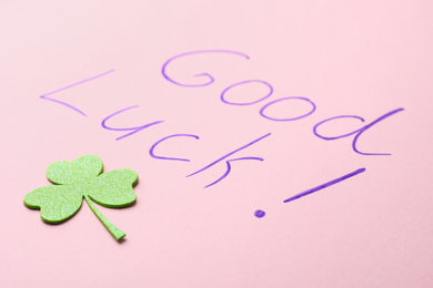 Photo of Phrase GOOD LUCK and clover leaf on pink background, closeup