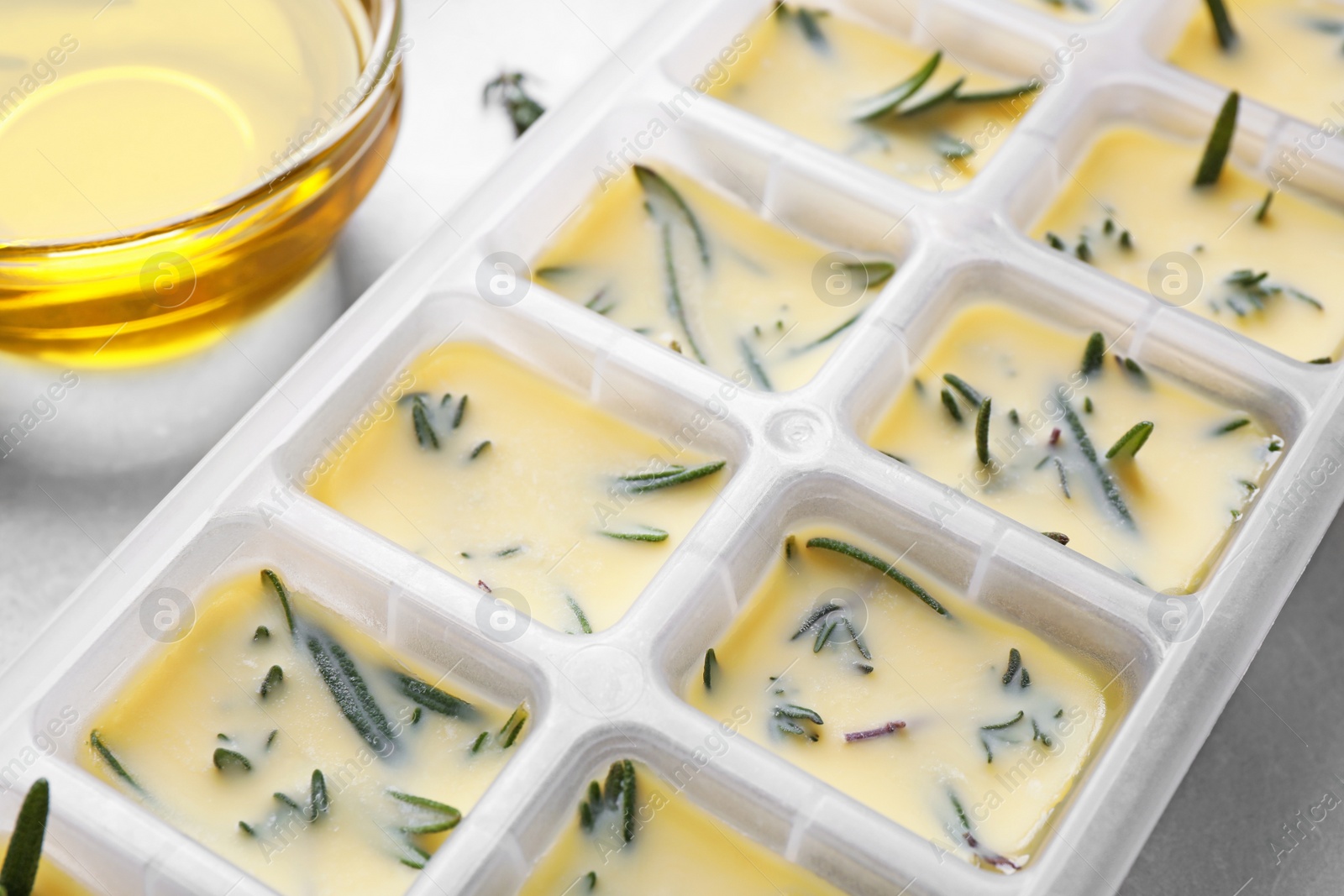 Photo of Ice cube tray with herbs frozen in oil and fresh rosemary on grey table, closeup