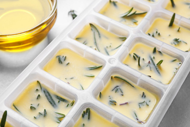 Photo of Ice cube tray with herbs frozen in oil and fresh rosemary on grey table, closeup